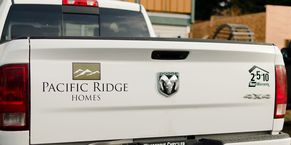 Tailgate of a white Dodge truck with "Pacific Ridge Homes" logo and "2-5-10 Year Warranty" sticker.