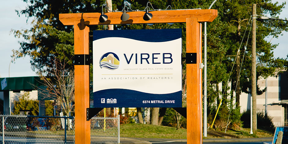 Sign for VIREB (Vancouver Island Real Estate Board) at 6374 Metral Drive, mounted on a wooden frame with lights and trees in the background.