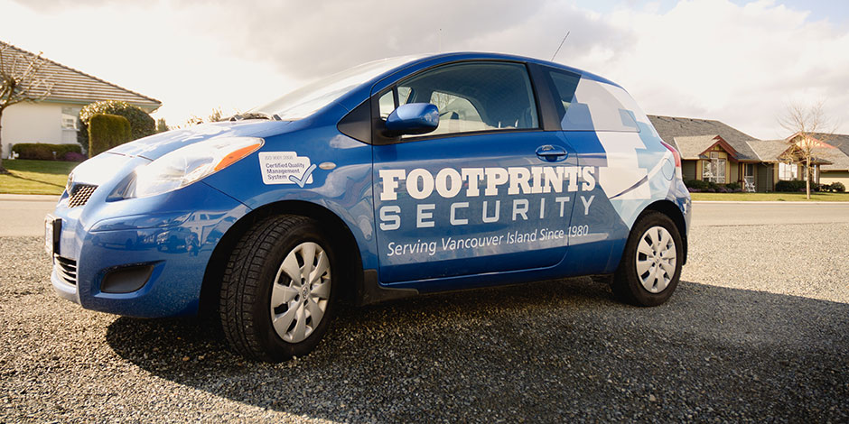 A blue car with "Footprints Security" and a badge reading "Better Business Bureau certified" is parked on a residential street on a sunny day. The car service is noted as serving Vancouver Island since 1980.