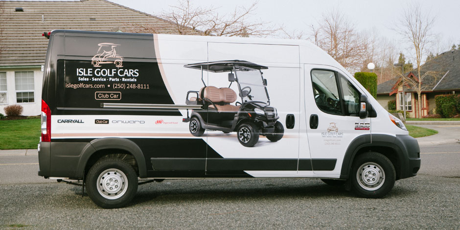 White commercial van with a company's advertisement on the side, showcasing a golf cart. Text includes "Isle Golf Cars," contact information, and logos of brands. The van is parked on a residential street.