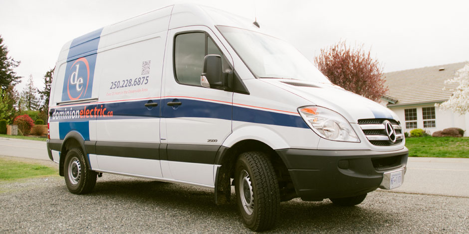 White Mercedes-Benz Sprinter van with "domainelectric.ca" and contact number painted on the side, parked on a residential street.