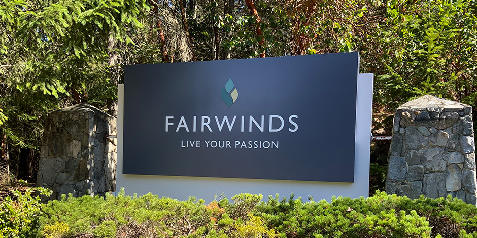 A sign with "Fairwinds Live Your Passion" displayed in front of a background of trees and bushes.