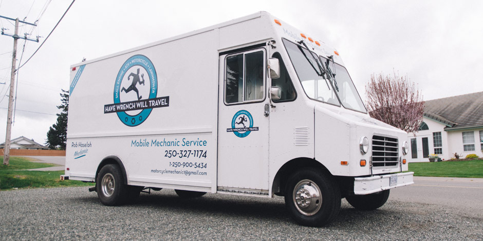 White mobile mechanic service truck with "Have Wrench Will Travel" logo, contact number, and email address parked on a suburban street near houses.