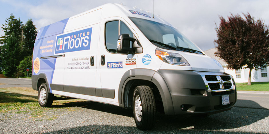 A white and blue van with "United Floors" branding is parked on a grassy area near a road, with trees and houses in the background. The van displays contact information and services provided.