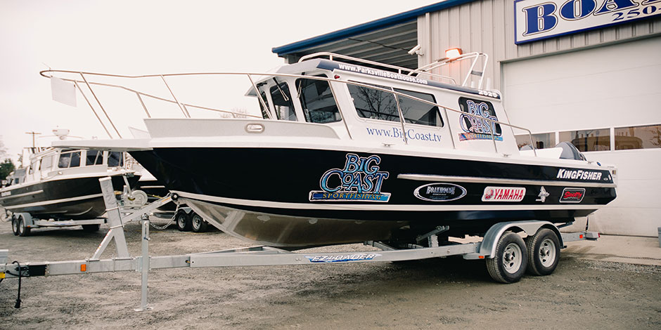 A KingFisher boat on a trailer parked outside a building with "Big Coast" graphics and several sponsor logos.