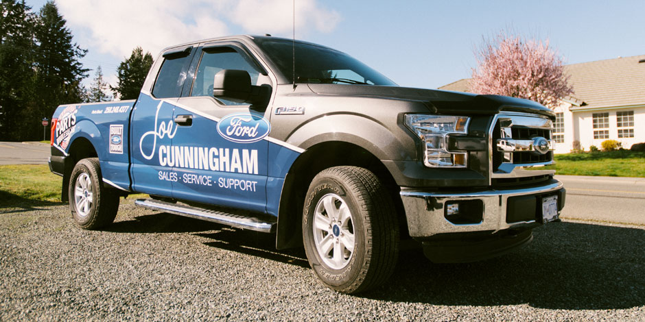 A Ford pickup truck parked on a gravel driveway. The truck features 'Cunningham Sales - Service - Support' branding on the side. Trees and a house are visible in the background.