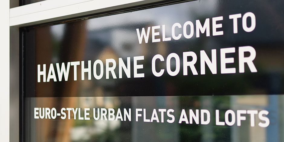 Sign reading "Welcome to Hawthorne Corner - Euro-Style Urban Flats and Lofts" displayed on a glass window.