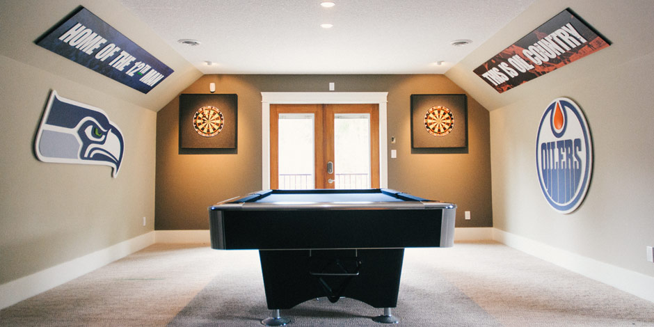 A game room featuring a pool table, two dartboards, and sports team signs on the walls. Natural light comes in from double doors at the back.