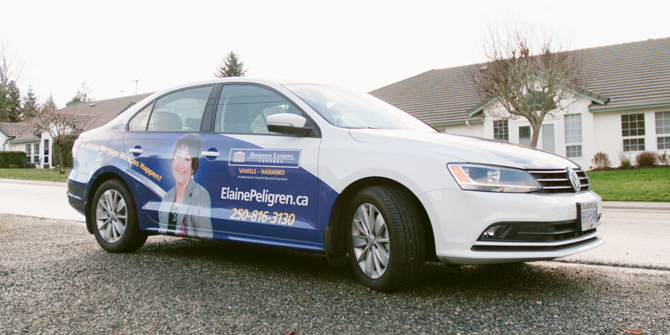 A white sedan with an advertisement for a real estate agent on its side, parked on a residential street. The ad includes a photo of a woman and contact information.