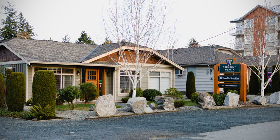 Single-story building with a sign for "Precision Wealth" and "Manulife Securities" surrounded by landscaped shrubs, rocks, and trees.