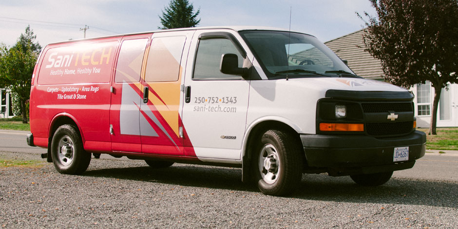 A red and white van with "Sani Tech" branding is parked on a gravel surface. The van features the company's contact number and services offered, such as carpet and upholstery cleaning.