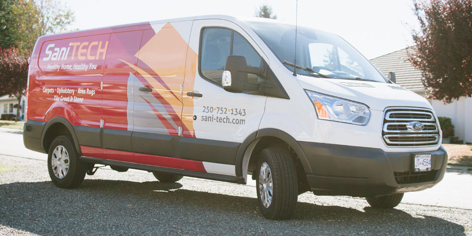 A white Ford van with "SaniTECH" branding is parked on a street. The van displays a phone number, website, and services like carpet and upholstery cleaning.