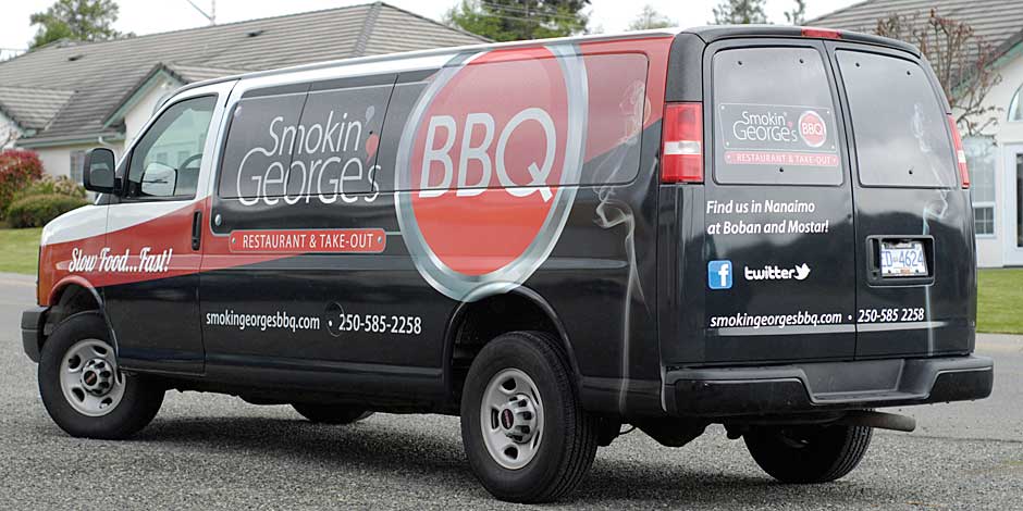 A black van with "Smokin' George's BBQ" branding, including contact information and social media handles, is parked on a residential street.