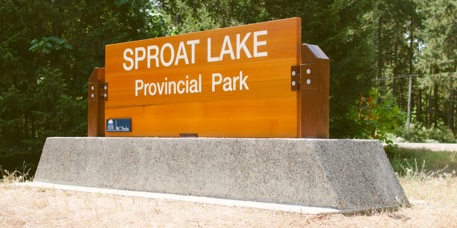 Sign for Sproat Lake Provincial Park in a wooded area, mounted on a concrete base.