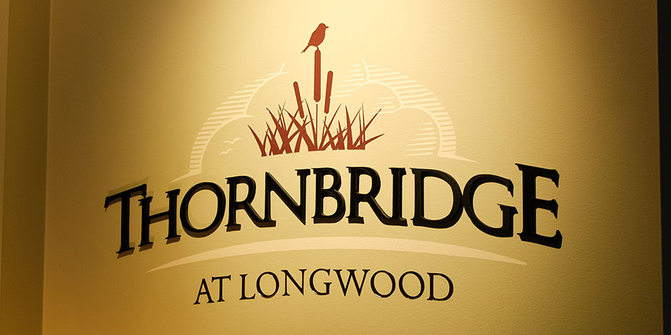 Thornbridge at Longwood" logo with a bird perched on cattails in the background, displayed on a beige wall.