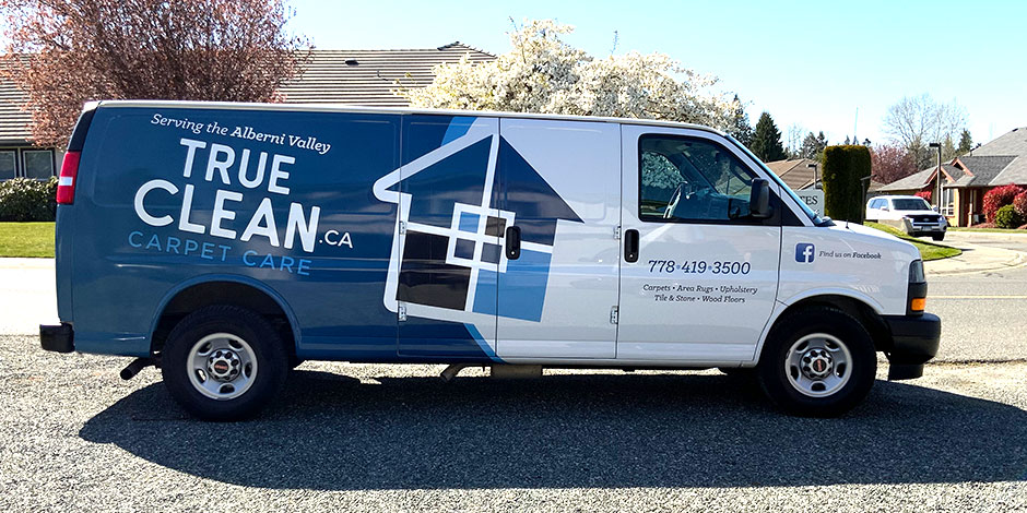 White and blue van for "True Clean Carpet Care" with logo and contact information parked on a sunny residential street.