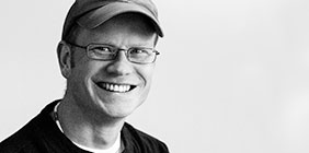 Wes Cargill wearing glasses and a cap smiles at the camera against a plain background.